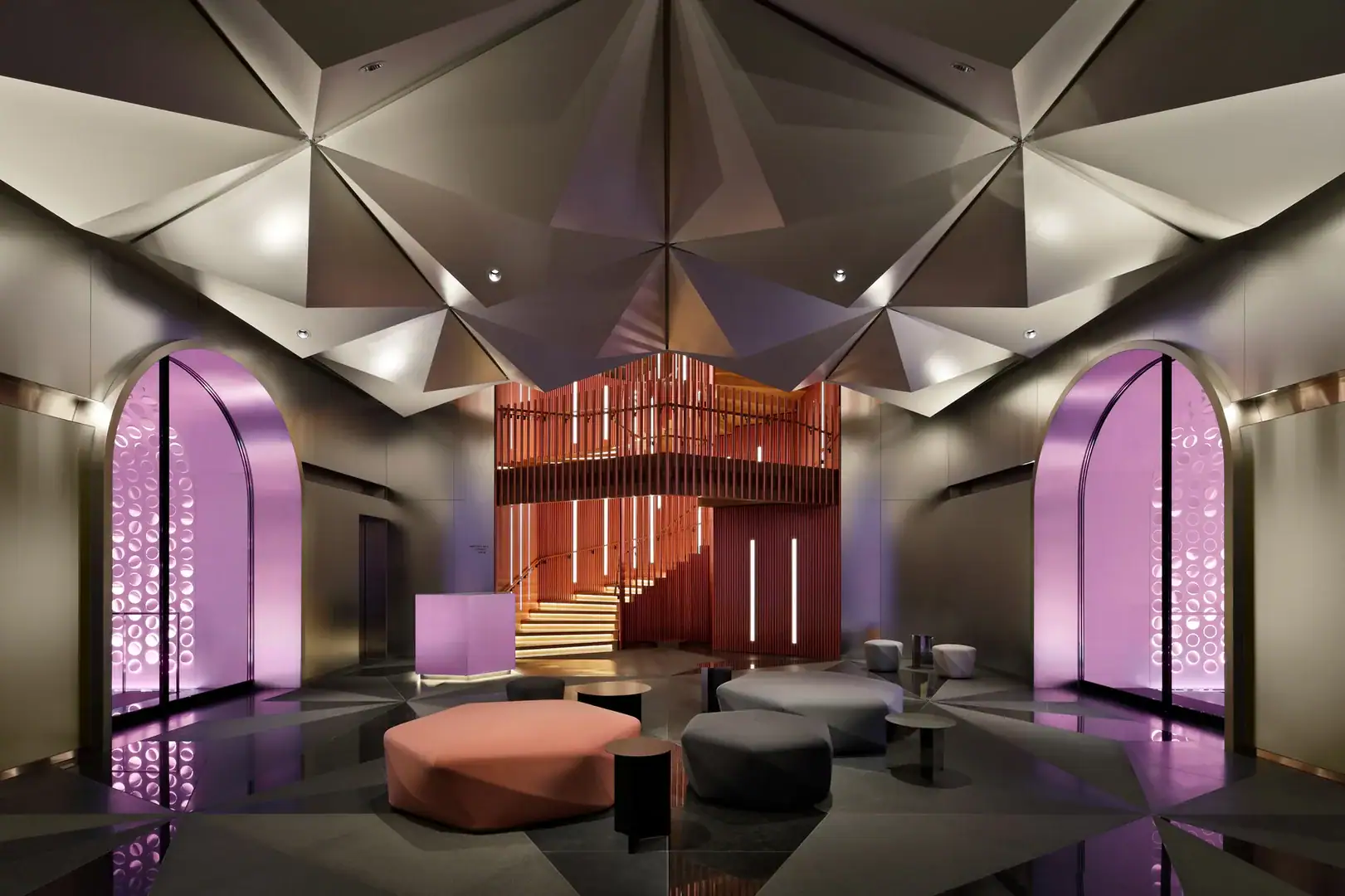 Lounge with two corridors with pink lightning on each sides, modern seating area in orange, grey and black and spiral staircase in orange.
