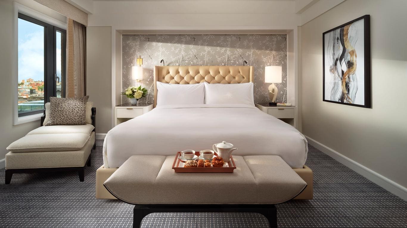 A suite with a king sized bed, a painting on the left side o the wall. WIth some tea and cafe in front of the bed.