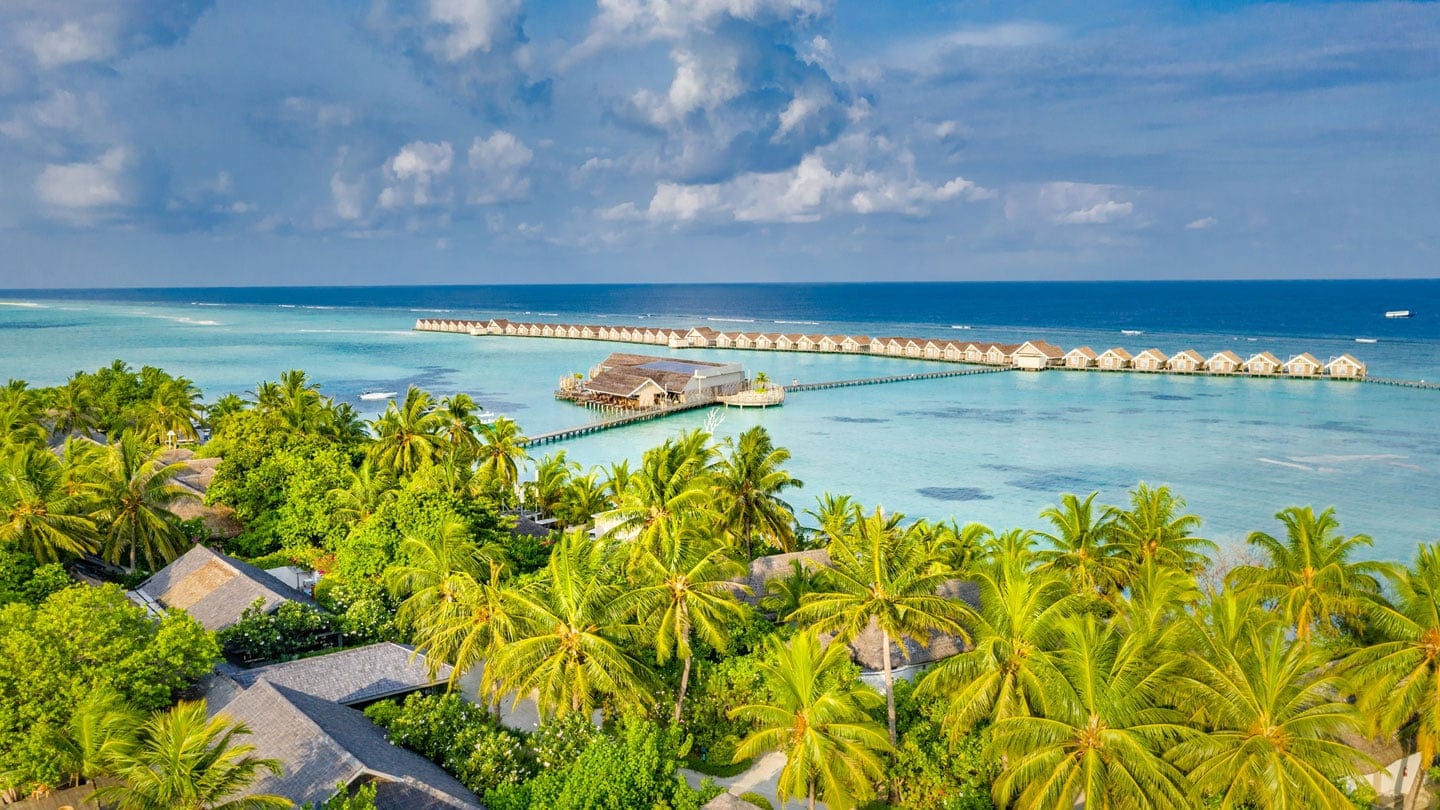 Bird view of LUX South Ari Atoll with palm trees, cabins in the island, cabin extensions to the water at LUX South Ari Atoll.