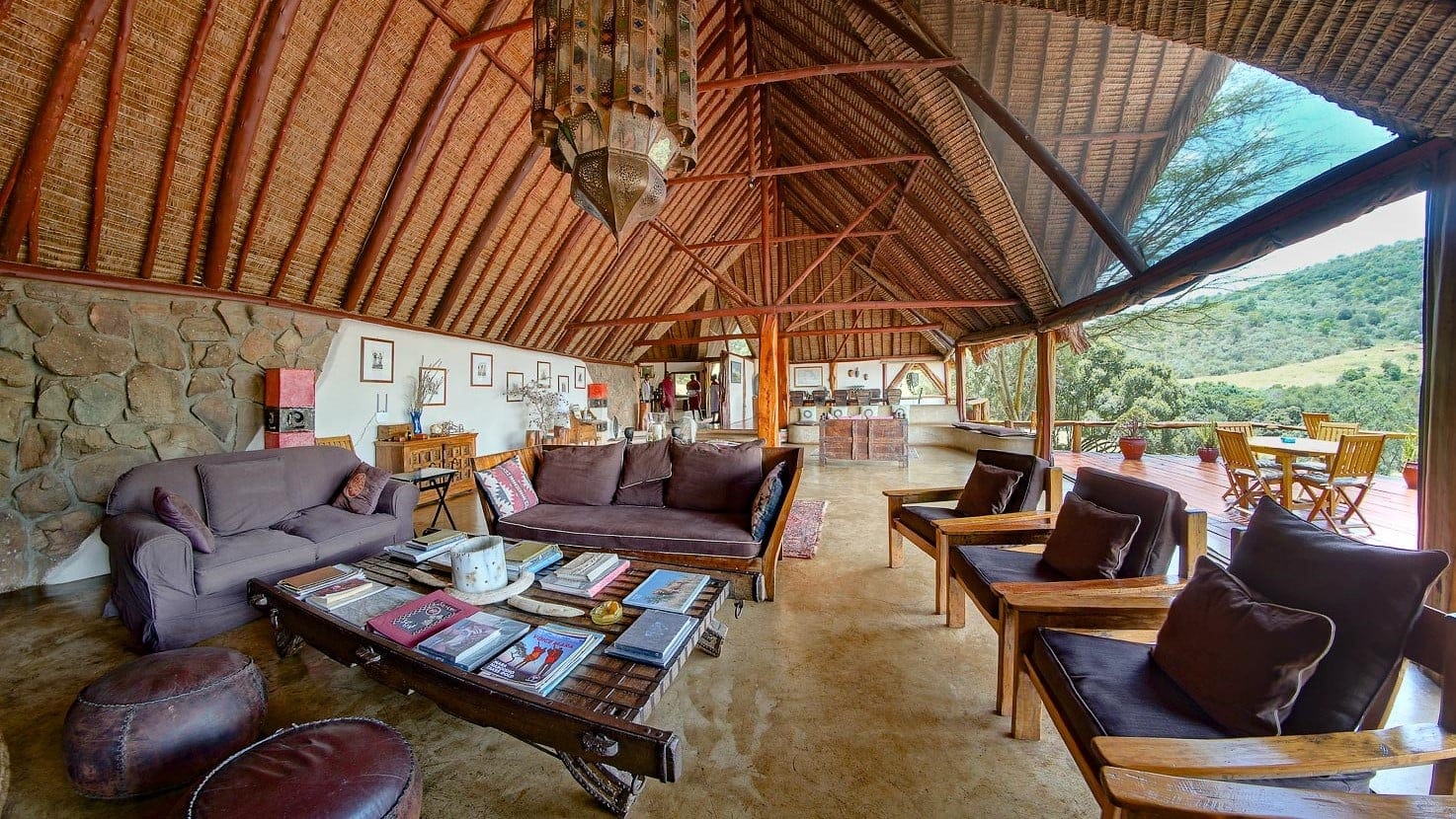 Large lounge with books, art, leather chairs and sofas and open exit to a terrace with nature view