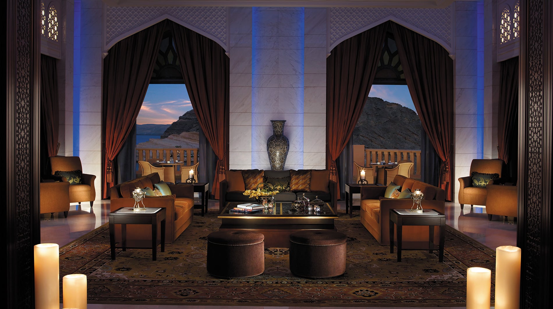 Living room with brown sofas, marble walls and large windows out to beutiful mountains and oceans
